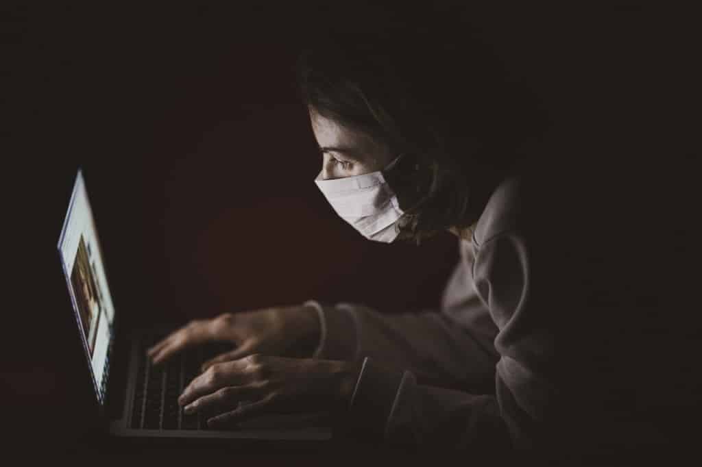 dziewczyna z maseczką siedząca w ciemności przed komputerem